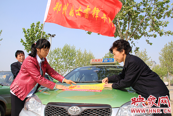 　　授旗結(jié)束后，首都的士雷鋒車隊王鳳進隊長（右）與鄭州的的哥的姐在車身上貼上標識。
