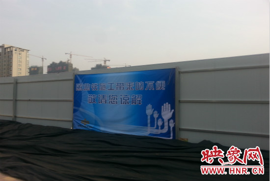 道路南側(cè)圍起了白色的圍擋，墻上標(biāo)示著“因地鐵施工帶來的不便敬請您諒解”的提示牌。