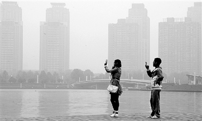 29日中午，鄭東新區(qū)如意湖畔，兩個(gè)年輕人拍攝霧霾中的景色。 鄭州晚報(bào)記者 馬健 圖