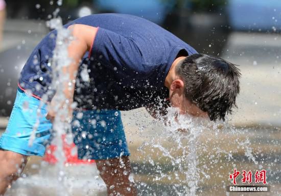 5月29日，一名小孩將頭伸向北京街頭的噴泉以降溫祛暑。