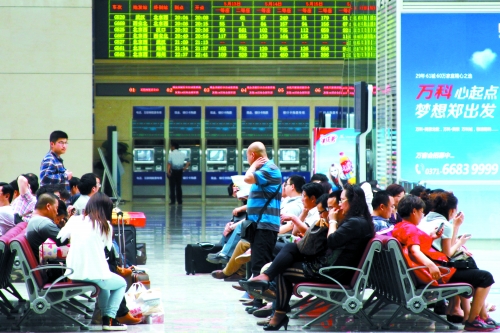 候車大廳溫度很高，一名乘客一手扇風(fēng)、一手擦汗