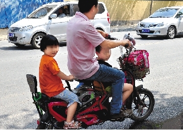周先生騎著一輛低矮的電動(dòng)車帶著一對(duì)兒女，很不安全。
