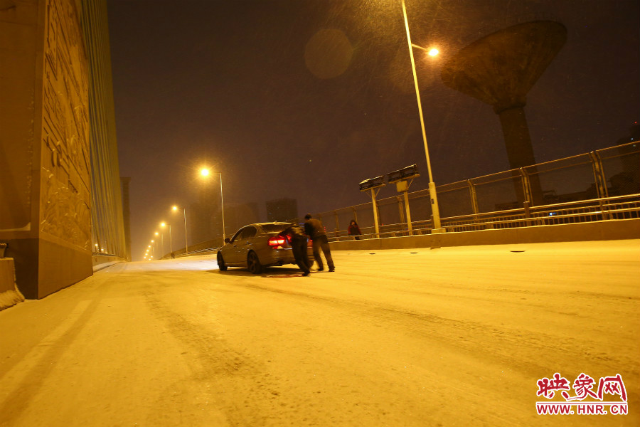 雪天路滑，汽車上橋打滑，兩名“推車人”幫助一輛私家車上坡。