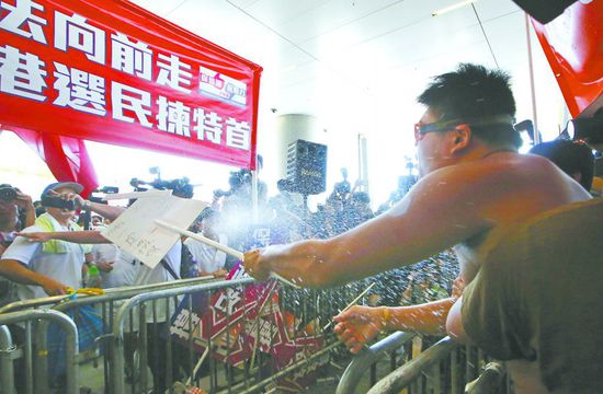17日，在香港立法會(huì)外，一名反對政改的男子向支持派人群投擲標(biāo)牌。