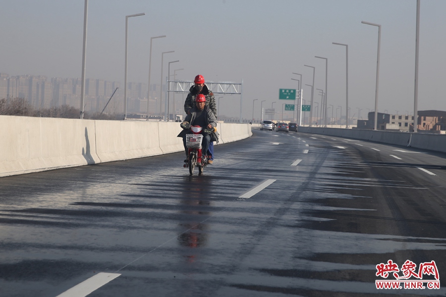 兩名工人騎車(chē)經(jīng)過(guò)灑水養(yǎng)護(hù)路面。