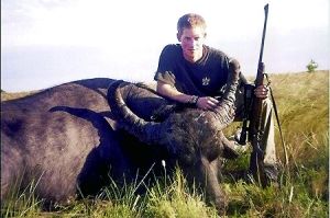 哈里王子手持獵槍，蹲在一頭遭到獵殺的水牛旁邊
