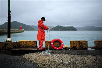 7月6日，韓國(guó)珍島，一名海岸警察在港口系救生圈。4月，客輪在珍島近海發(fā)生沉船事故后，仍有11人下落不明。