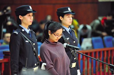 被告人盧梅低著頭，站在朝陽法院刑事審判庭的被告席上。